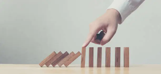 Photo of Hand stopping wooden domino business crisis effect or risk protection concept