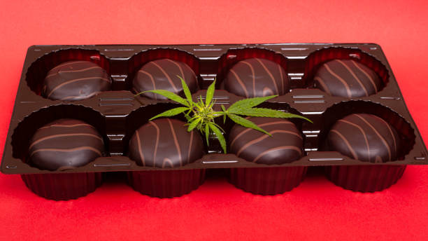 box of chocolates and green leaf of cannabis on red background box of chocolates and green leaf of cannabis on red background. bud candy stock pictures, royalty-free photos & images