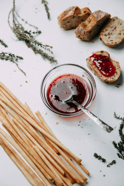 istock Slices of white bread on a white background. Raspberry jam with a towel. Gresini with thyme in Flatley layout. 1202642734