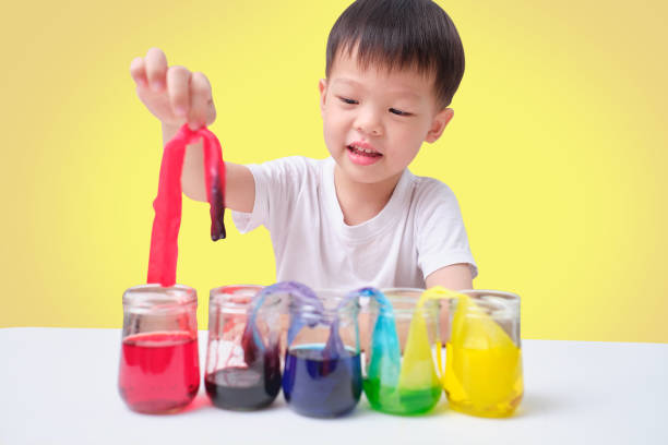 istock Asian toddler boy making Color Changing Walking Water Experiment, Glasses in row with colored water and wet paper between, Easy Kids Science Experiment concept 1202642821