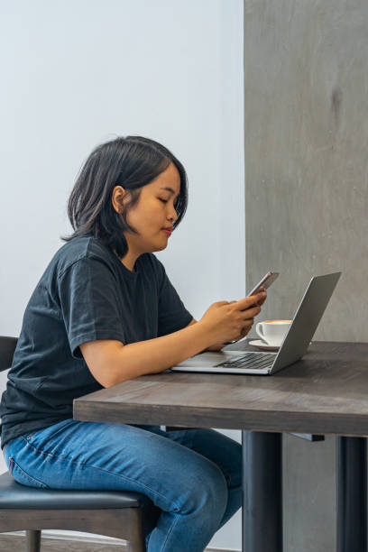 femme asiatique utilisant le smartphone et l’ordinateur portatif à l’atelier de café - brown table coffee table side table photos et images de collection