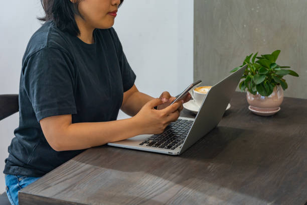 femme moderne asiatique utilisant le smartphone et l’ordinateur portatif au café - brown table coffee table side table photos et images de collection