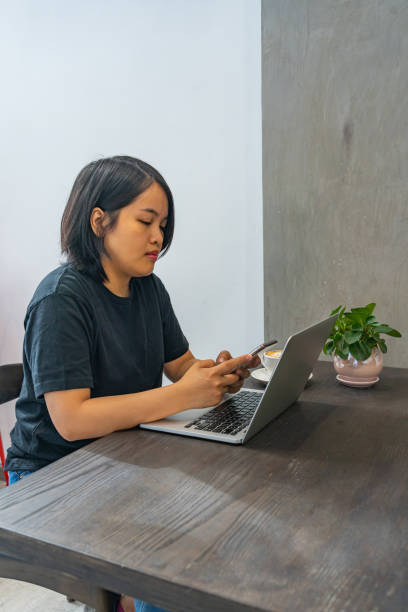 pigiste féminin asiatique utilisant le smartphone et l’ordinateur portatif au café - brown table coffee table side table photos et images de collection