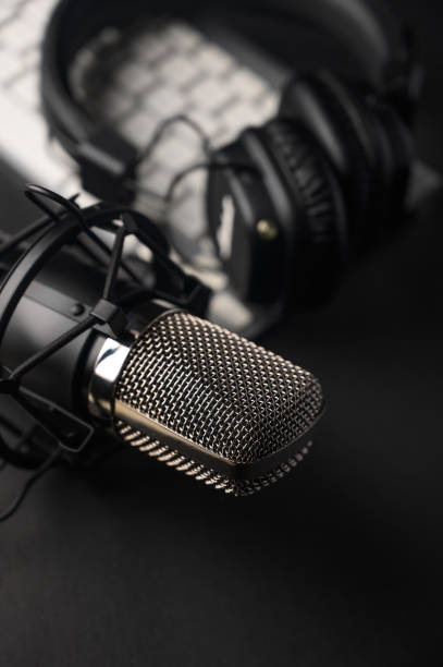 istock Microphone for podcasts and studio headphones on a PC keyboard on a black background, vertical frame 1202650309