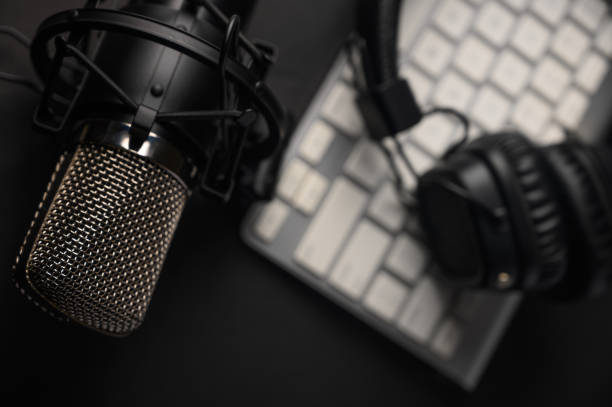 istock Microphone for podcasts and studio headphones on a PC keyboard on a black background, horizontal frame 1202650376