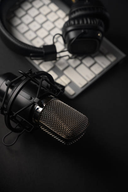 istock Microphone for podcasts and studio headphones on a PC keyboard on a black background, vertical frame 1202650440