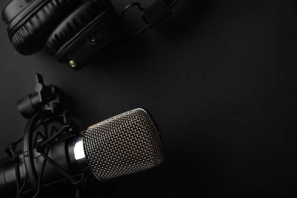 istock Studio black studio microphone with studio headphones on a black background. Banner. Radio, work with sound, podcasts. 1202651626