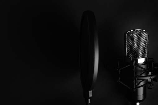 Black studio microphone on a black background with a pop filter with space for design