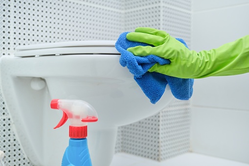 Close-up of woman hand in gloves with rag and detergent washing hanging toilet, home cleaning in bathroom