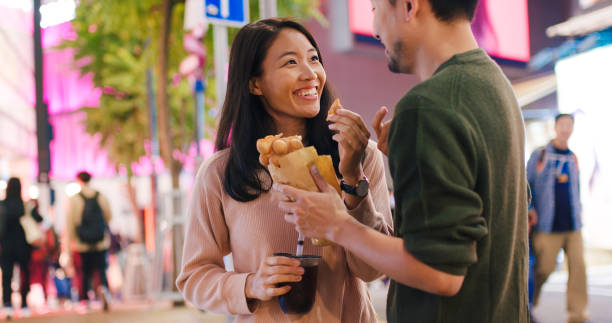 istock Young couple enjoying egg waffles and bubble tea outdoors at night 1202657179