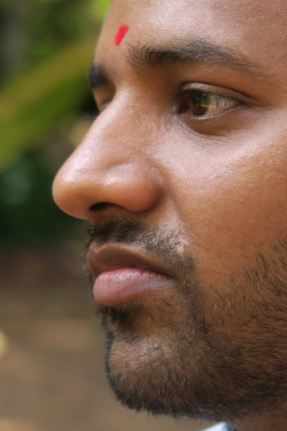 istock Image of happy young Indian Hindu man looking serious with red bindi drop dot on forehead, third eye bindu worn by Hindus and Jains coloured with scarlet red vermilion powder, handsome young man in India with short beard stubble in jungle 1202660514