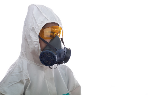 Portrait of hardworking female employee in protective workwear and respirator looking at camera while standing indoors