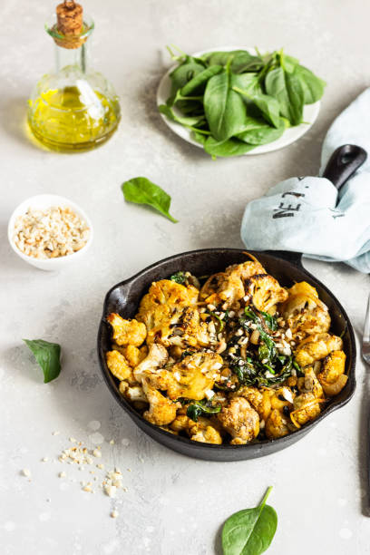 istock Roasted cauliflower with spinach, raisin and nuts in a cast-iron pan. Light grey background. Copy space. Healthy vegan food. 1202666392
