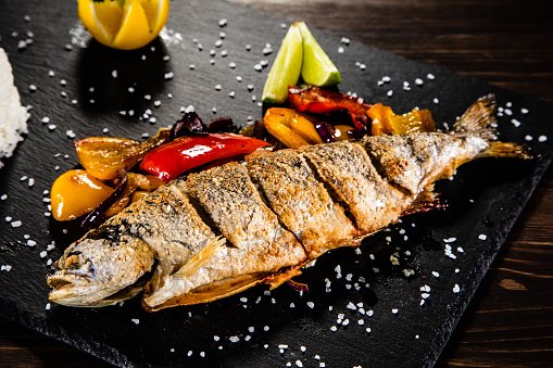 Fried trout with rice and vegetables on wooden background