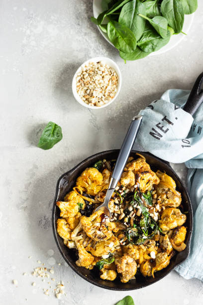 istock Roasted cauliflower with spinach, raisin and nuts in a cast-iron pan. Light grey background. Copy space. Healthy vegan food. 1202666424