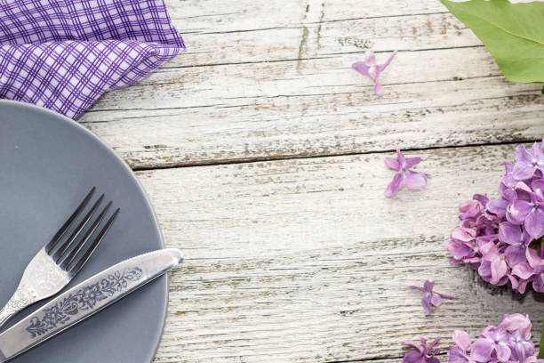spring table setting with plate fork and knife decorated with lilac flowers on white wooden background. Top view with copy space