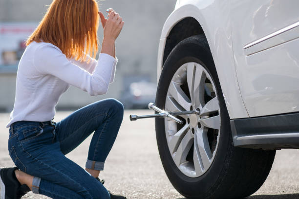 istock Young woman with wrench changing wheel on a broken car. 1202672047