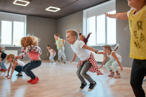 Group of cute little boys and girls studying modern dance in studio. Children jumping while having a choreography class. Sport. Active lifestyle