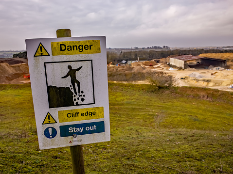Danger sign warning of a cliff edge with an out of focus chalk quarry in the distance
