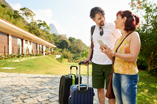 Shot of a traveler couple standing at a holiday resort with their luggage using a phone