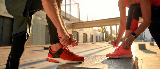 Active morning. Close up photo of two people in sport clothes tying shoelaces before running together outdoors. Fit, fitness, exercise. Healthy lifestyle concept