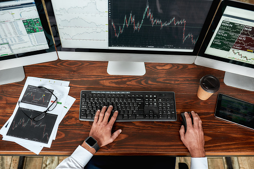 Top view of businessman, trader working, sitting by desk in front of multiple computer monitors. Stock trading forex with technical indicator tool. Hands on keyboard. Horizontal shot