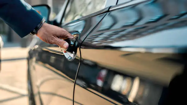 Cropped photo of a male hand opening the door of a black car while standing outdoors. Close up. Transportation