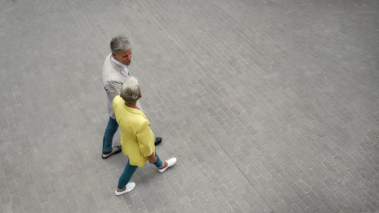 Top view of stylish mature couple holding hands and walking together through the city street. Relationships. Spending time together. Middle-aged couple