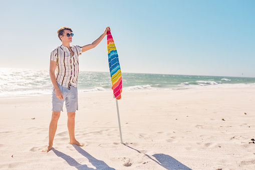 Full length shot of a handsome young man posing next to his beach umbrella at the beach
