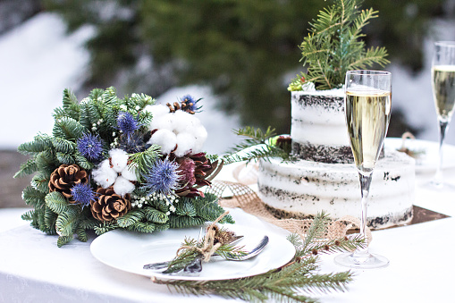 Rustic winter wedding. Table decor. Winter wedding table decor bride and groom for photo shoot. Aerial view of winter green garland on a wedding table with white plates, cake, glasses, champagne.