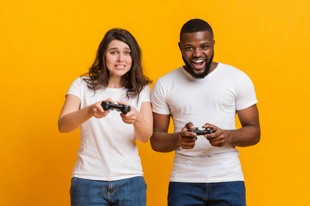 istock Gambling multiracial couple playing videogames with joysticks, posing over yellow background 1202683167