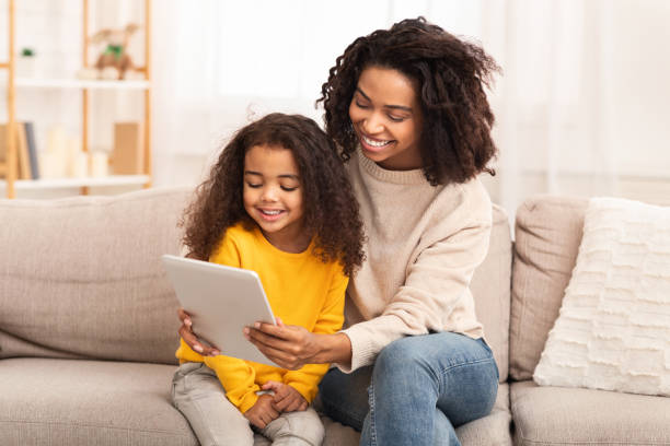 istock Mother And Daughter Using Tablet Watching Cartoons Sitting On Couch 1202684827