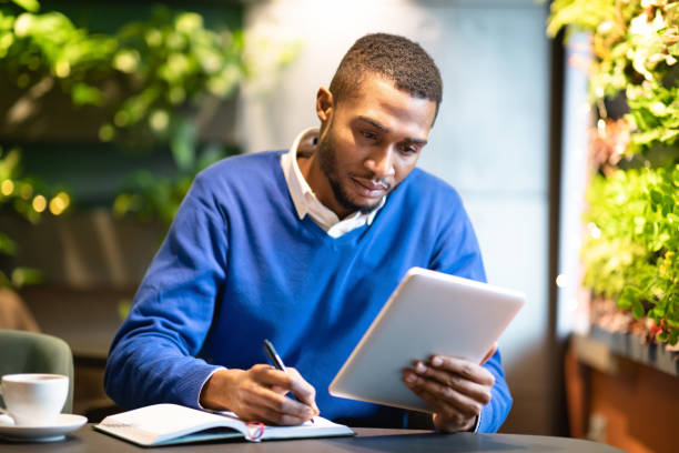 черный человек, держащий планшет и пишущий в блокноте - e reader digital tablet cafe reading стоковые фото и изображения