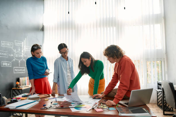istock Perfect teamwork. Professional team of young web designers working on a new project together and discussing ideas while standing in the modern and bright office 1202685378