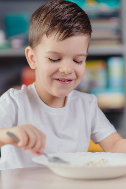 istock The child has breakfast with oatmeal porridge. The boy eats while sitting at a table in the kitchen at home. 1202686559