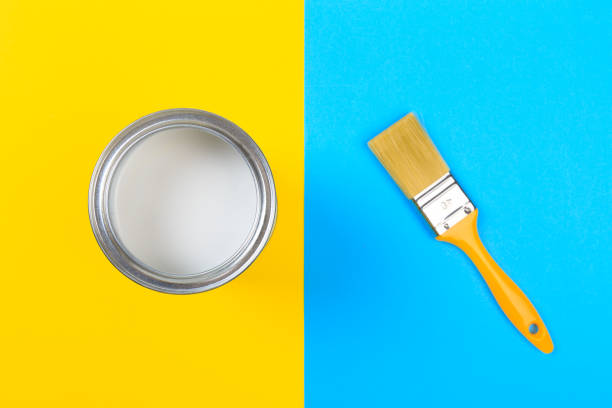 istock White Paint Can with Brush Top View On Yellow and blue  Background. 1202687136