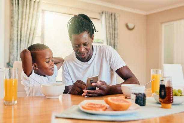 Should we go to this park later? Cropped shot of a happy father and son bonding over breakfast and technology during a weekend at home carbohydrate food type stock pictures, royalty-free photos & images