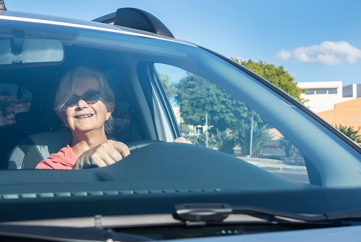 Senior woman smiling while parking the car. Looking at the rear view mirror. View from outside the car. Caucasian senior female.