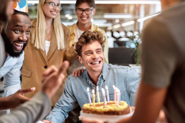 頑張ってください。笑顔の混血のビジネスマンの間で誕生日を祝いながらケーキにろうそくを吹く若い幸せな男 - cake birthday candle blowing ス��トックフォトと画像