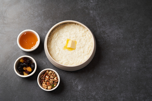 Rice porridge with milk, raisins, honey and nuts in a bowl. Healthy breakfast - milk rice porridge in a white plate on grey table background, close-up