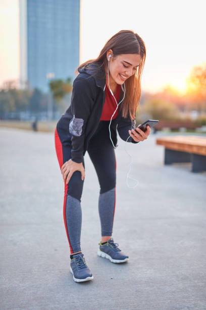 Modern young woman with cellphone making pause during jogging / exercise.