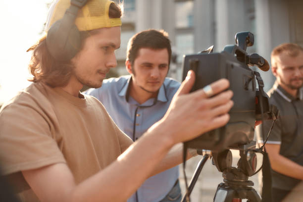 Close up portrait of young professional cameraman in headphones, recording a video footage using a professional dslr camera and tripod. Horizontal shot. Side view