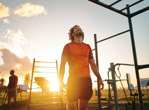 Happy fit young man enjoying listening to music on earphones after exercising in the outdoor gym park on summer sunny day Relaxed cheerful male sportive young man in gym park gym men africa muscular build stock pictures, royalty-free photos & images