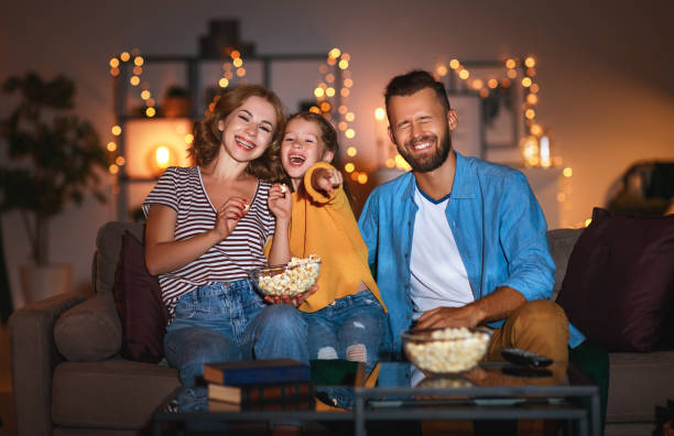 ojciec matki rodziny i córka dziecka oglądania projektor, telewizja, filmy z popcornem w godzinach wieczornych w domu - projection equipment home interior house living room zdjęcia i obrazy z banku zdjęć