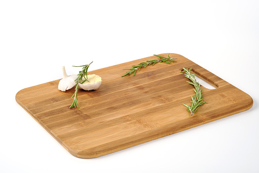 A wooden cutting board made of bamboo on a white background. A place for a product. Vegetables and greens and large salt as decoration.