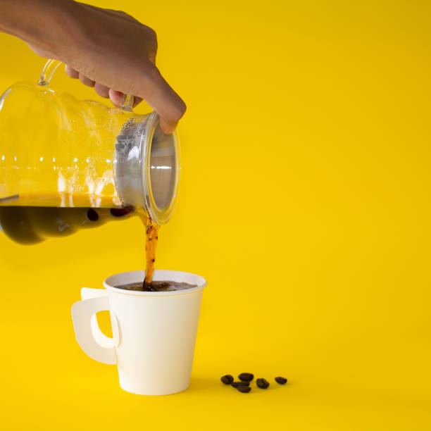 istock Hand holding  coffee pouring into white cup on yellow paper background. Copy space for your text 1202693513