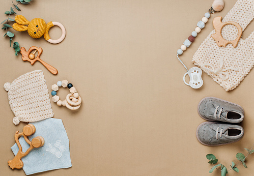 Eco baby clothes and accessories concept. Wooden toys, clothes and shoes on beige background with blank space for text. Top view, flat lay.