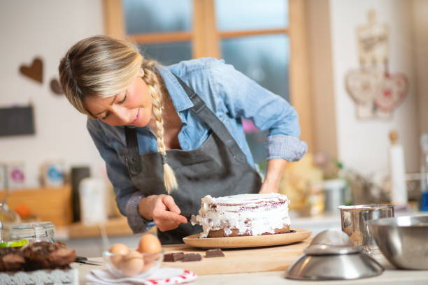 istock Woman baking at home: Spreading whipped cream on chocolate sponge cake 1202697709