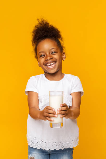 smiling black little girl holding glass of milk - milk child drinking little girls imagens e fotografias de stock