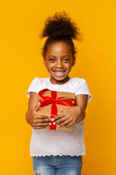 istock Cheerful afro girl holding gift box, yellow background 1202699103